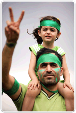 Un uomo con una bambina sulle spalle, entrambi con fasce verdi alla testa, fa il segno di vittoria durante una manifestazione a Tehran